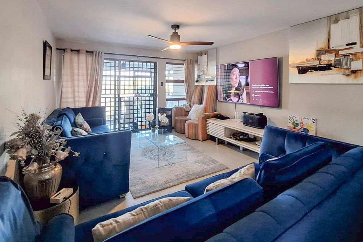 A comfortable living room featuring laminate flooring, a ceiling fan, and a sliding glass door with security gate leading to an outdoor area.