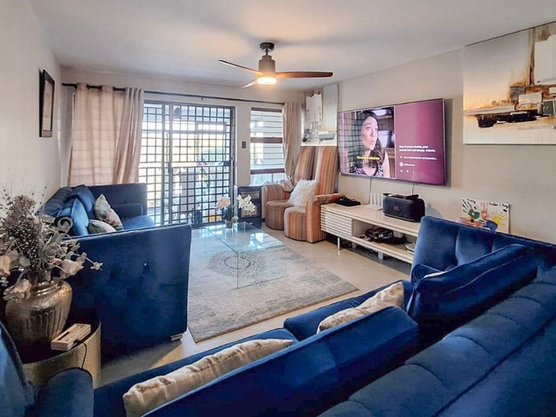 A comfortable living room featuring laminate flooring, a ceiling fan, and a sliding glass door with security gate leading to an outdoor area.