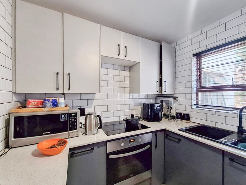 Modern kitchen featuring white subway tile backsplash, dark grey lower cabinetry, white upper cabinets, quartz countertops, and integrated oven with electric hob.