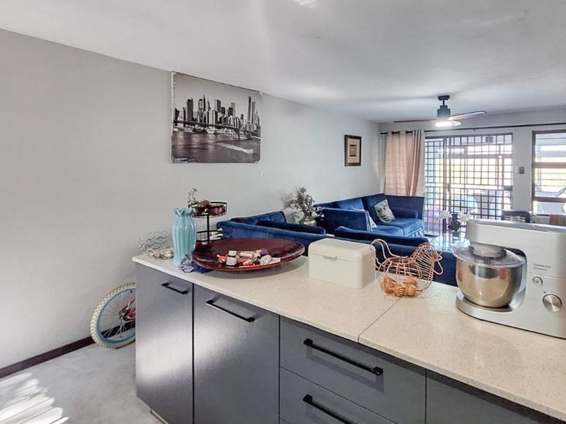 Open plan living area featuring a modern kitchen island with stone countertops, flowing into a comfortable lounge space with access to a secure patio.