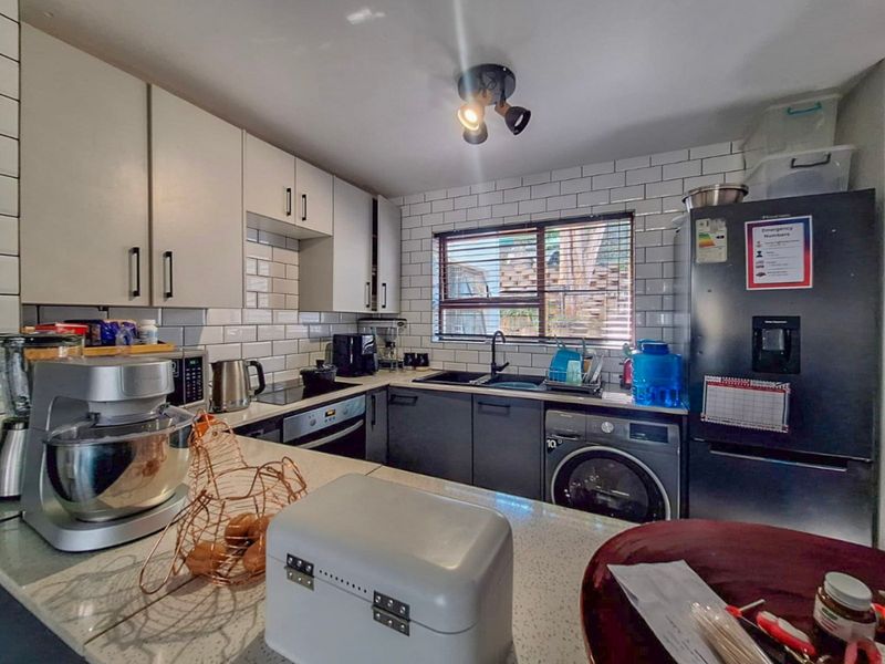 Modern kitchen featuring subway tile backsplash, stone countertops, built-in oven, hob, and integrated washing machine with ample cabinetry for storage.