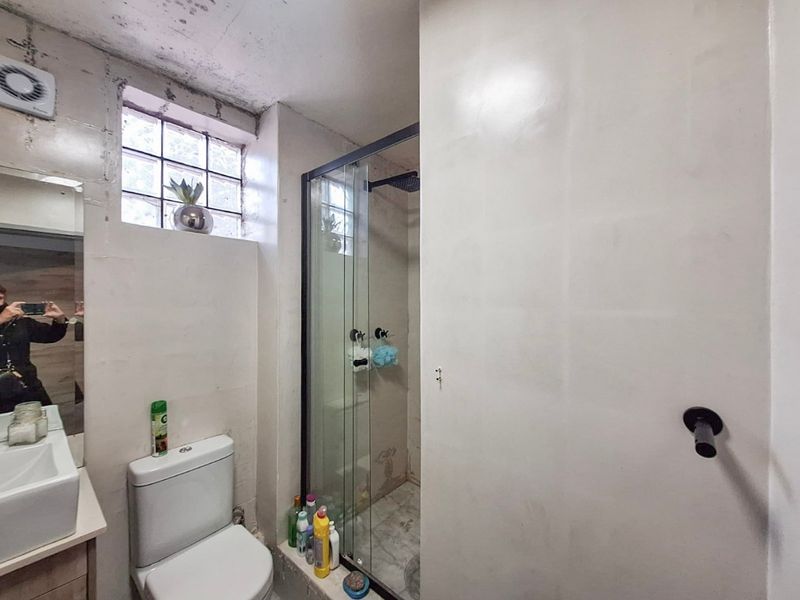 Compact bathroom featuring a glass shower enclosure, vanity basin, and toilet, with visible signs of ceiling water damage and unfinished wall surfaces.
