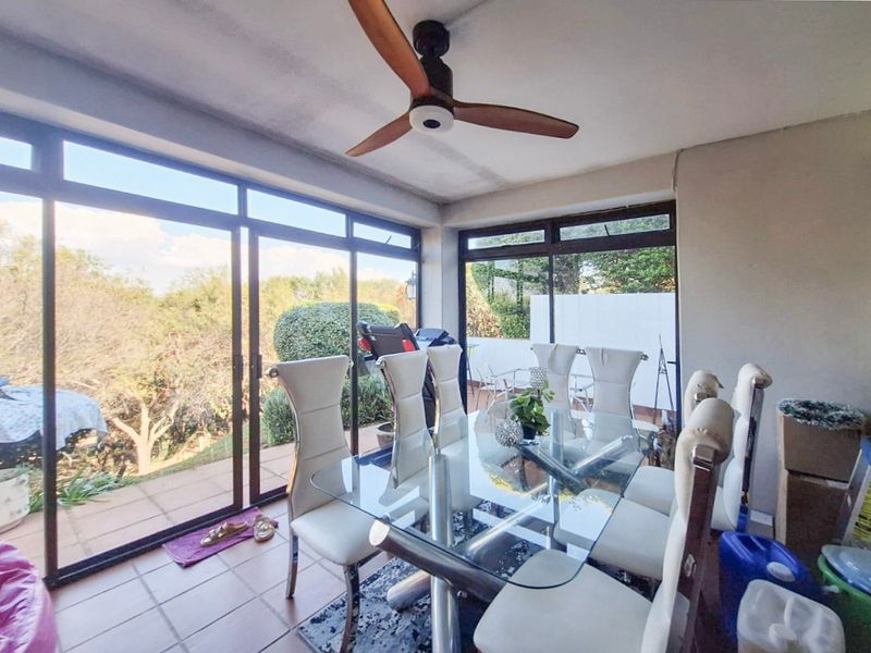 Enclosed patio area featuring large sliding glass doors, tiled flooring, and a ceiling fan, offering views of the surrounding garden.