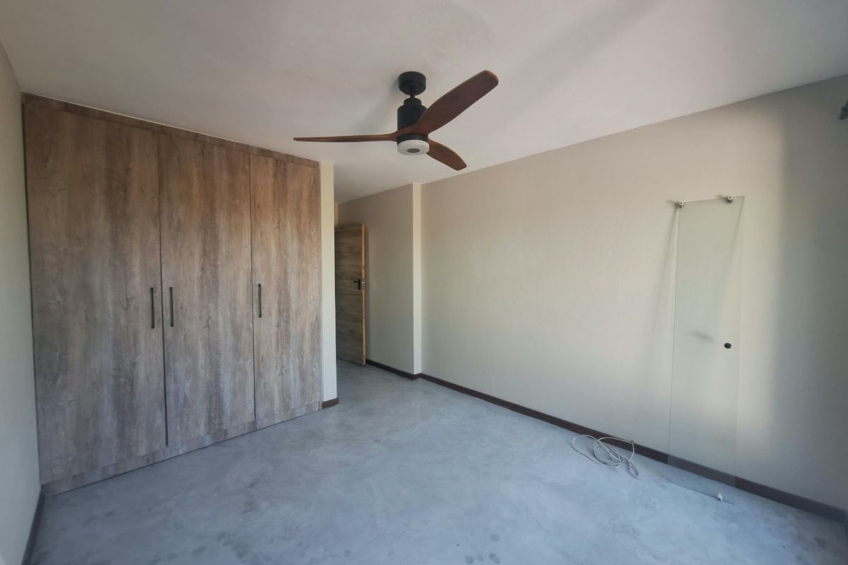An empty bedroom featuring built-in wood-look cupboards, a modern ceiling fan, and polished concrete flooring.