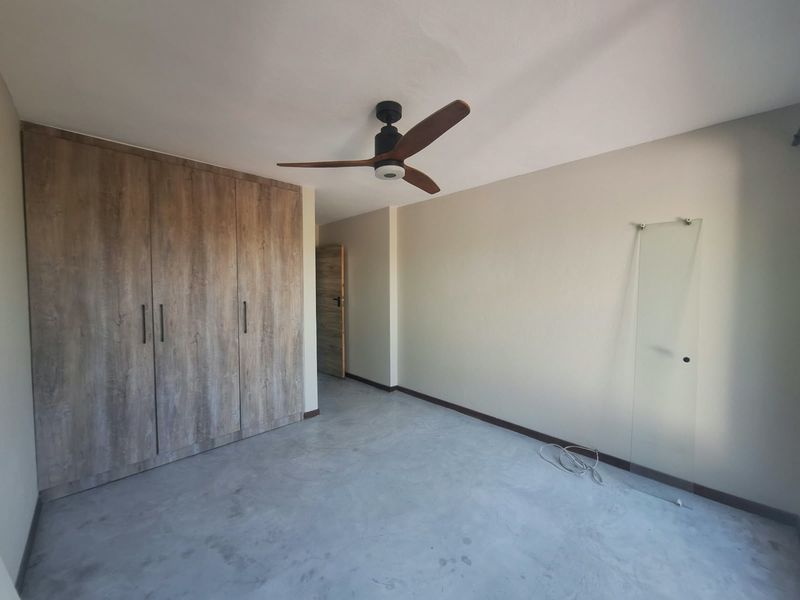 An empty bedroom featuring built-in wood-look cupboards, a modern ceiling fan, and polished concrete flooring.