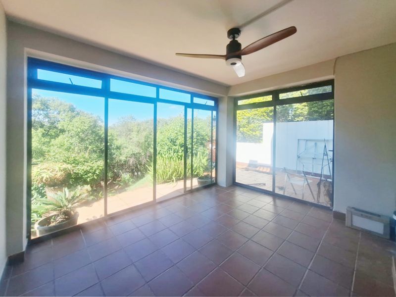 A spacious, empty enclosed patio featuring tiled flooring, a ceiling fan, and large sliding glass doors providing ample natural light and garden views.