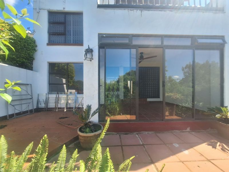 Rear exterior view of the apartment featuring a terracotta tiled patio, large sliding glass doors, and security-fitted windows.