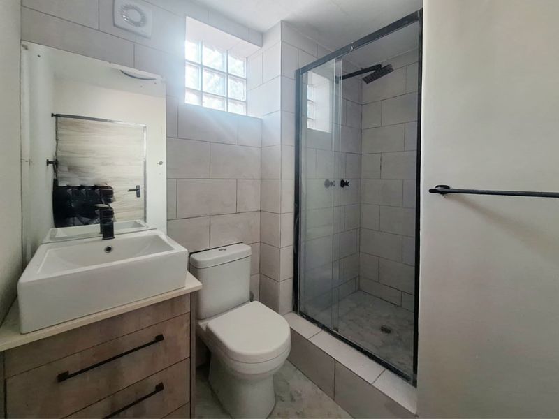 Modern bathroom featuring a vanity with vessel sink, toilet, and a glass-enclosed shower with contemporary black fixtures.