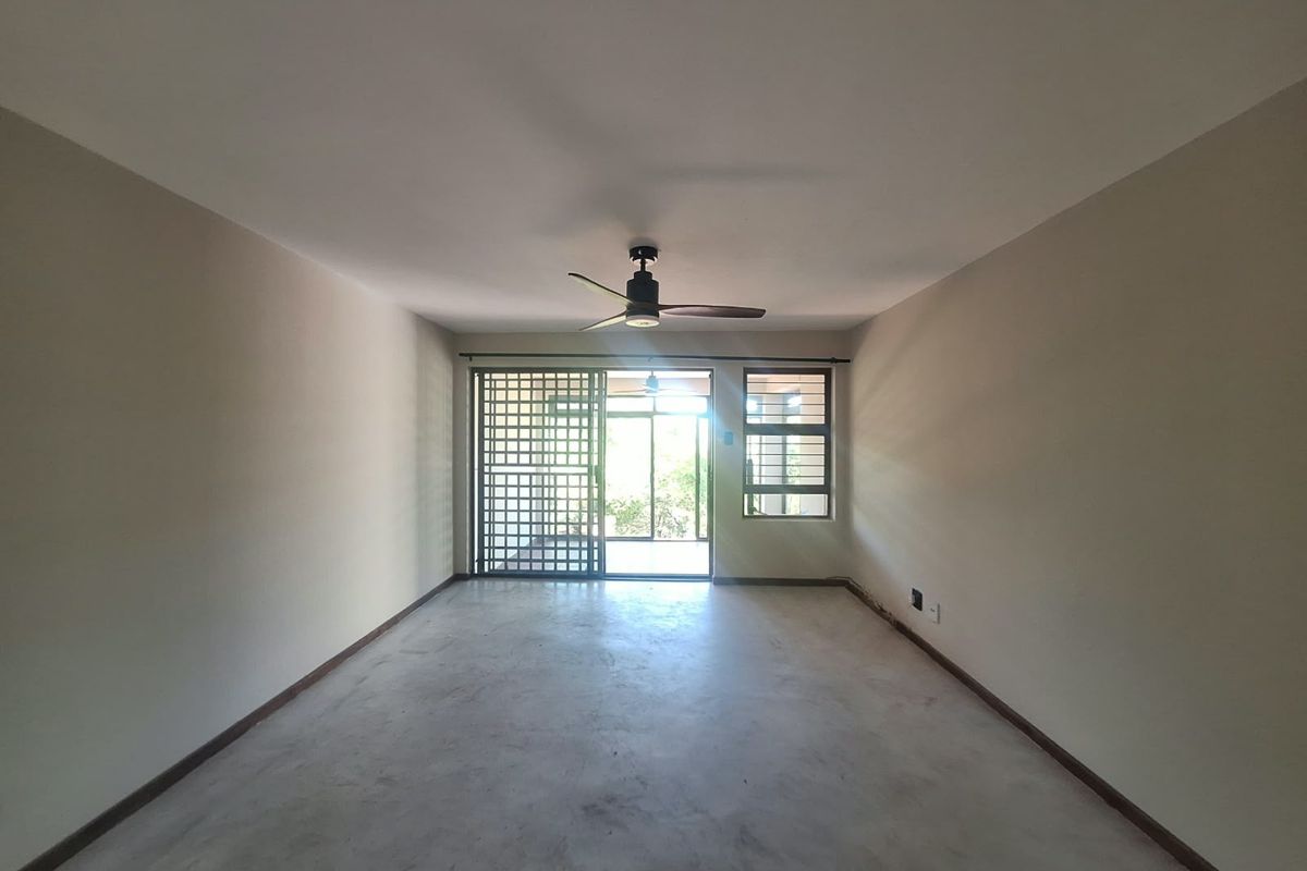 An empty, open-plan living area featuring a ceiling fan, sliding glass door with security gate, and large windows with security bars.