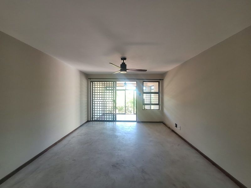 An empty, open-plan living area featuring a ceiling fan, sliding glass door with security gate, and large windows with security bars.