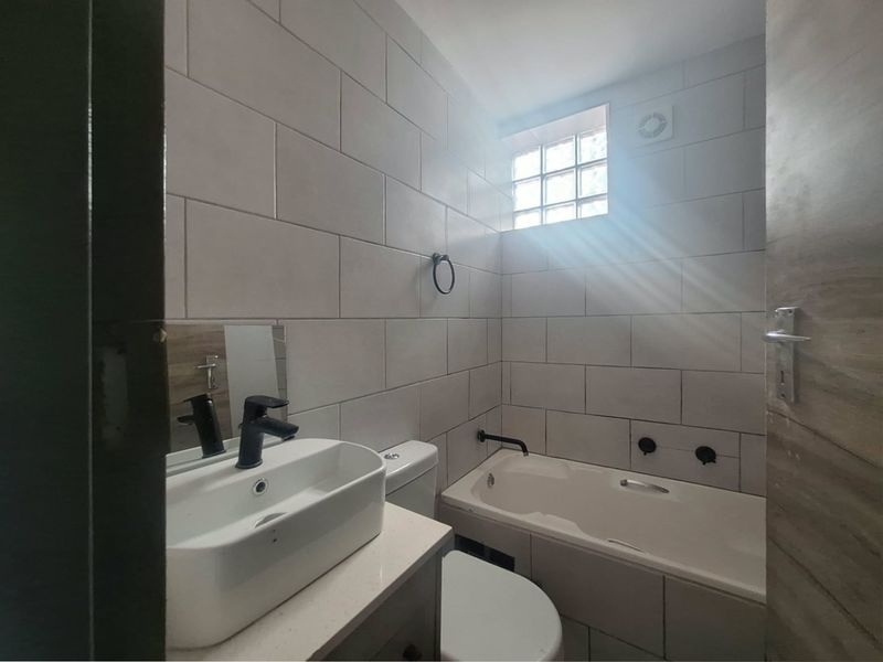 Modern bathroom featuring a vessel sink, vanity cabinet, bathtub with wall-mounted fixtures, and a glass block window for natural light.