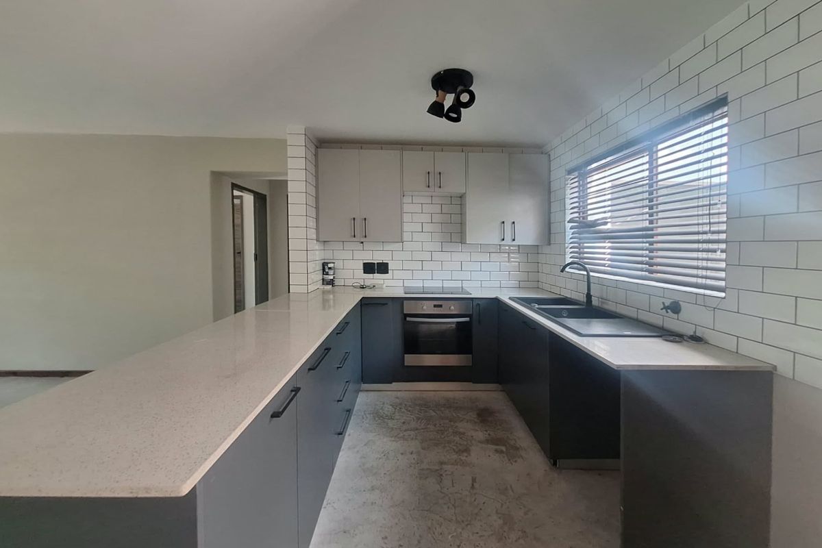 Modern kitchen featuring dark cabinetry, quartz countertops, subway tile backsplash, and integrated appliances, awaiting final flooring installation.