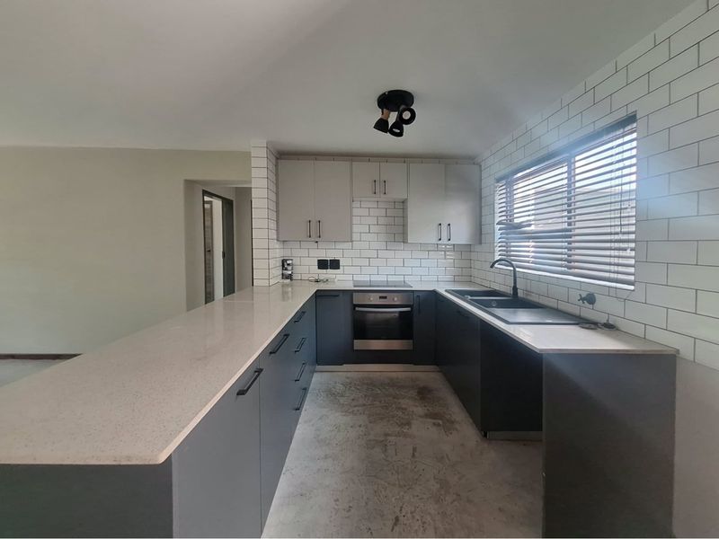 Modern kitchen featuring dark cabinetry, quartz countertops, subway tile backsplash, and integrated appliances, awaiting final flooring installation.