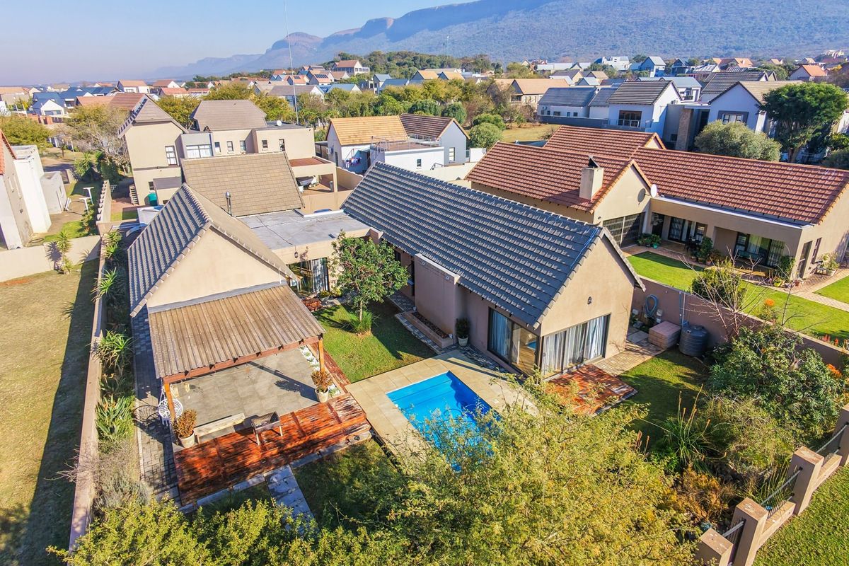Aerial view of a residential property featuring a swimming pool, wooden deck, covered patio, and landscaped garden within a suburban estate setting.