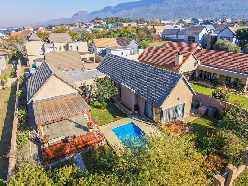 Aerial view of a residential property featuring a swimming pool, wooden deck, covered patio, and landscaped garden within a suburban estate setting.