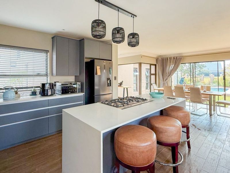 Modern open-plan kitchen featuring a central island with gas cooktop, sleek cabinetry, and seamless flow to the dining area and outdoor patio.