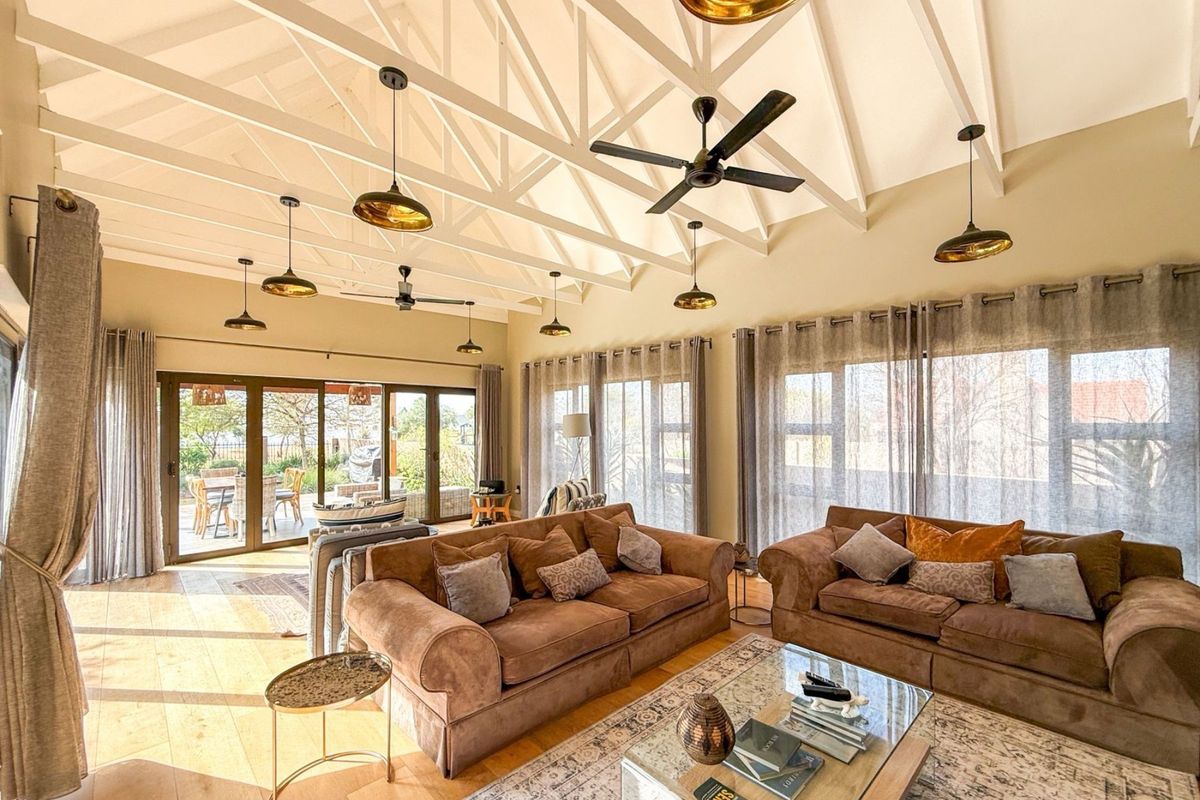 Spacious living room featuring a high vaulted ceiling with exposed trusses, multiple pendant lights, ceiling fans, and large sliding glass doors leading to the patio.