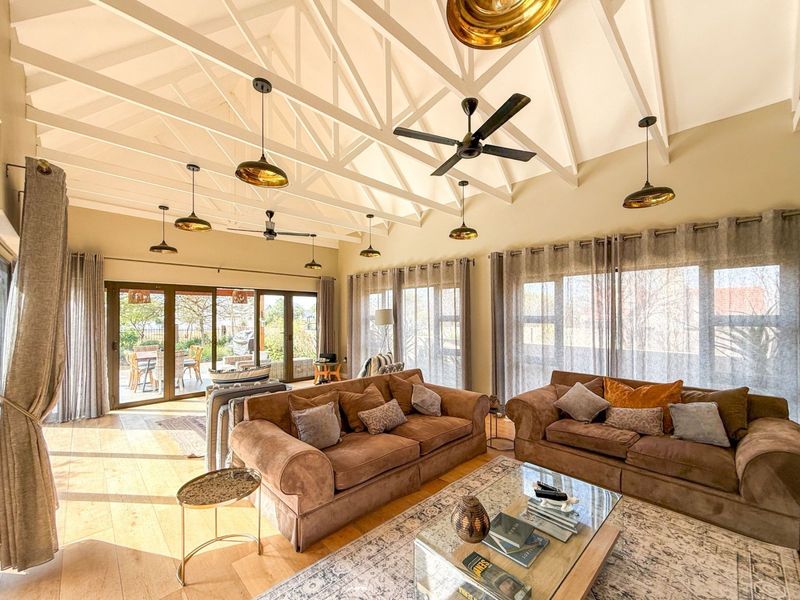 Spacious living room featuring a high vaulted ceiling with exposed trusses, multiple pendant lights, ceiling fans, and large sliding glass doors leading to the patio.