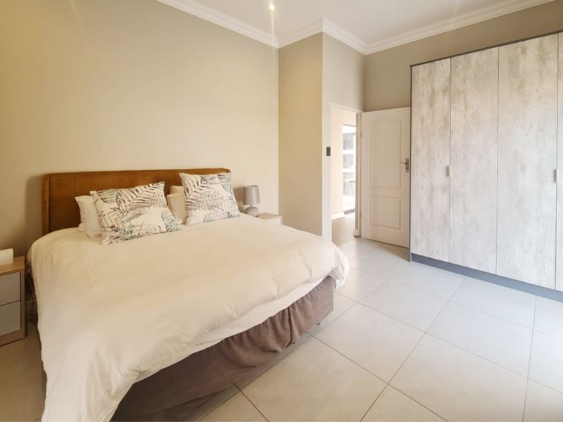 A well-maintained bedroom featuring neutral walls, tiled flooring, decorative cornicing, and modern built-in cupboards.