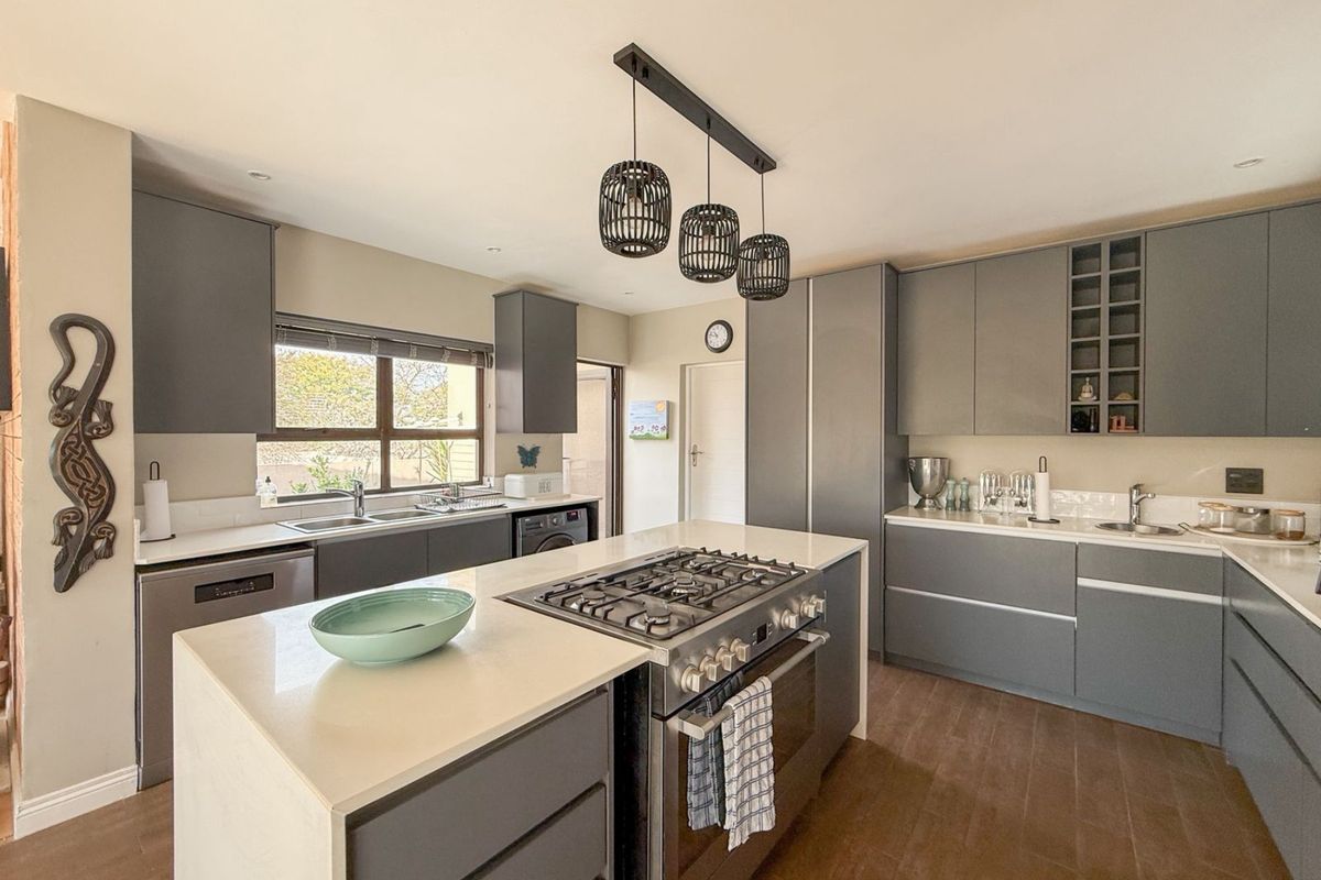 Modern kitchen featuring a central island with a gas cooktop, stone countertops, grey cabinetry, and integrated appliances, complemented by stylish pendant lighting.
