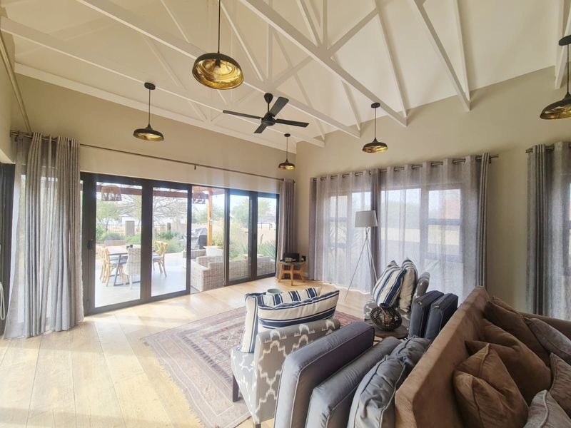 Spacious living room featuring a high vaulted ceiling with exposed trusses, timber flooring, and large sliding glass doors opening to an outdoor patio area.