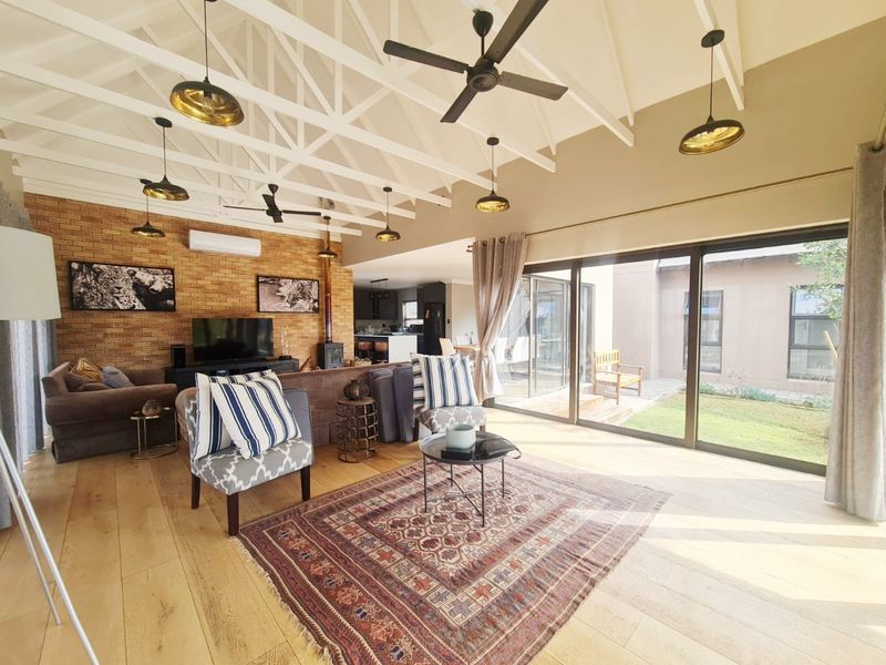 Spacious open-plan living area featuring exposed vaulted ceilings, a brick feature wall with fireplace, and large sliding doors opening to the garden.