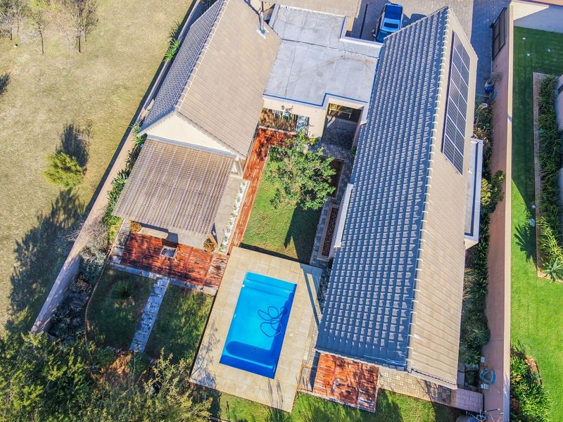 Aerial view of the property featuring a swimming pool, wooden decking, tiled roof with solar panels, and a landscaped garden area.