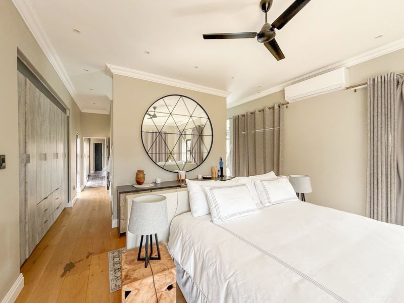 A well-appointed bedroom featuring timber flooring, built-in cabinetry, a ceiling fan, and a split-system air conditioner, finished with elegant cornicing and recessed lighting.