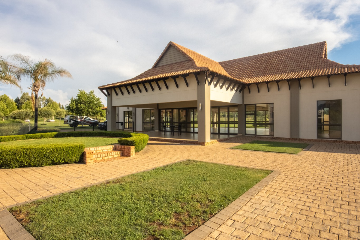 A well-maintained rear exterior view featuring a spacious paved courtyard, covered patio area, and neatly landscaped garden with established hedges.
