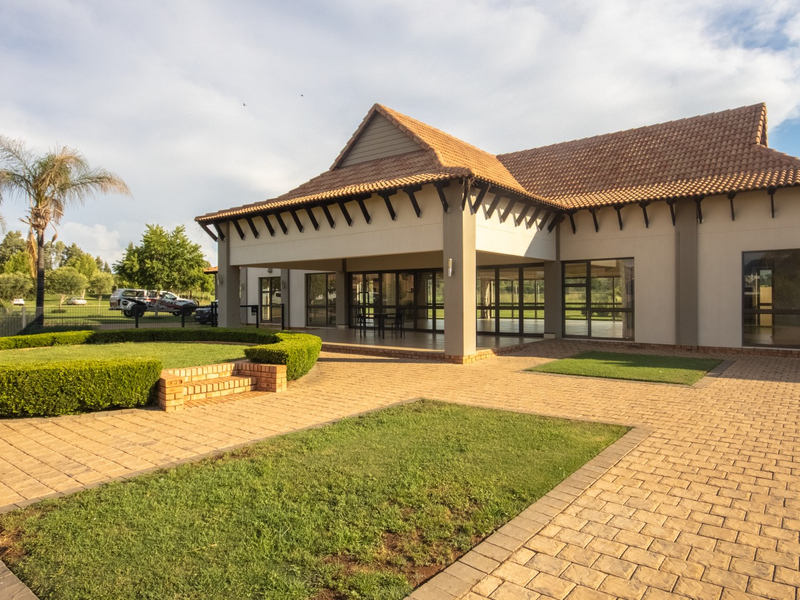 A well-maintained rear exterior view featuring a spacious paved courtyard, covered patio area, and neatly landscaped garden with established hedges.