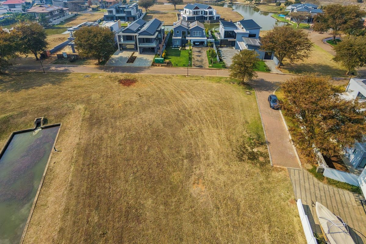 Aerial view of a vacant residential plot situated in a developed estate, featuring adjacent paved access and nearby water drainage infrastructure.