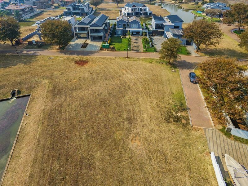 Aerial view of a vacant residential plot situated in a developed estate, featuring adjacent paved access and nearby water drainage infrastructure.