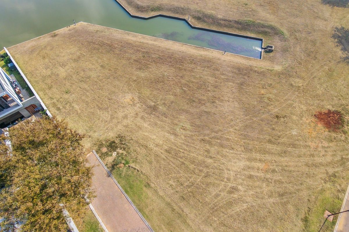 Aerial view of a vacant residential plot featuring a water feature, established grass, and adjacent paved access.