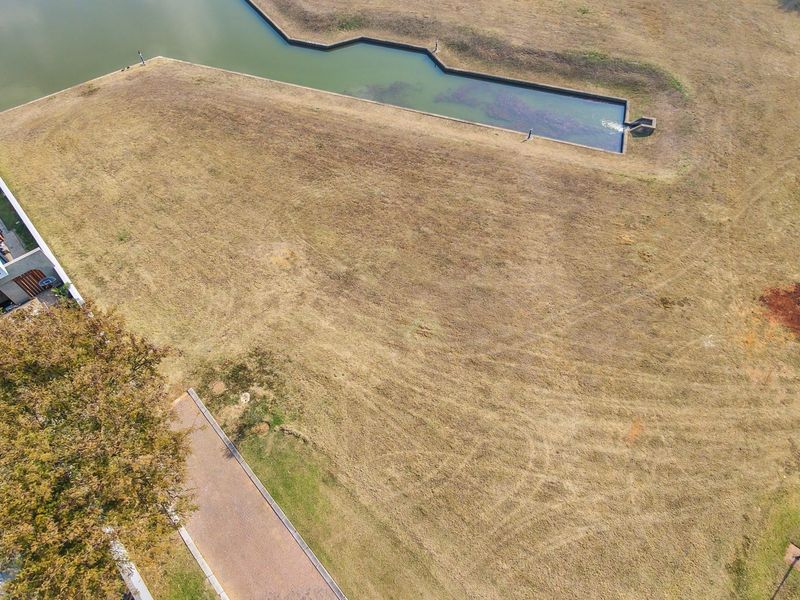 Aerial view of a vacant residential plot featuring a water feature, established grass, and adjacent paved access.