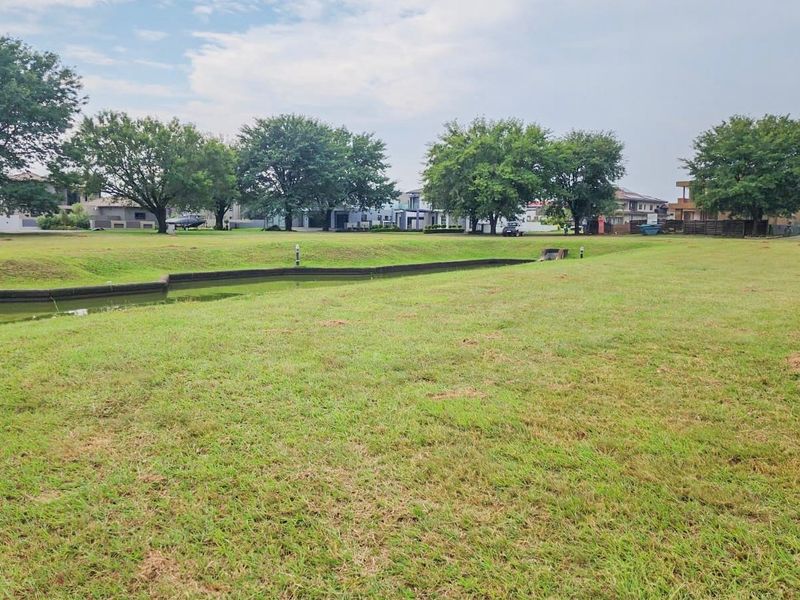 A spacious, well-maintained residential plot featuring a manicured lawn, mature trees, and a central water feature, offering a peaceful outlook.