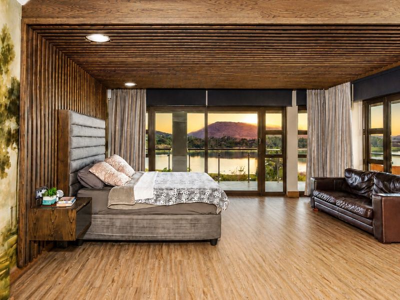 Spacious bedroom featuring warm timber slat ceilings and wall paneling, with expansive sliding glass doors offering scenic lake and mountain views.