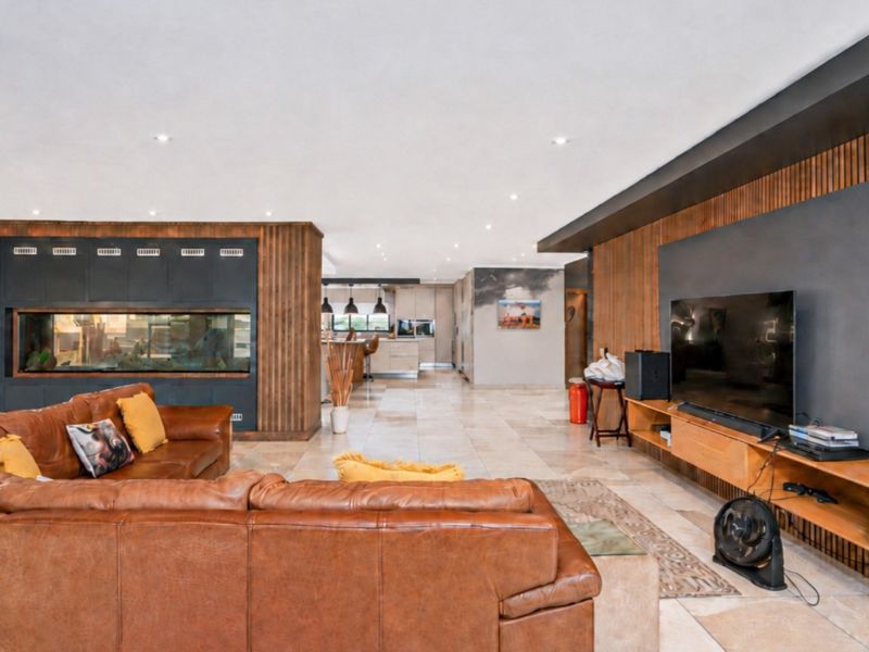 Spacious open-plan living area featuring high-end timber wall paneling, stone tile flooring, recessed lighting, and a unique built-in aquarium feature.