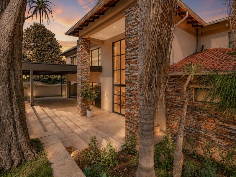 A striking modern home exterior featuring natural stone cladding, a tiled roof, and a spacious paved entrance area with integrated carport.