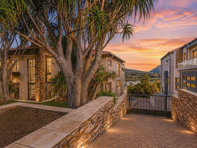 A beautifully landscaped front entrance featuring stone-clad retaining walls, a paved driveway, and modern architectural design with sunset views over the water.