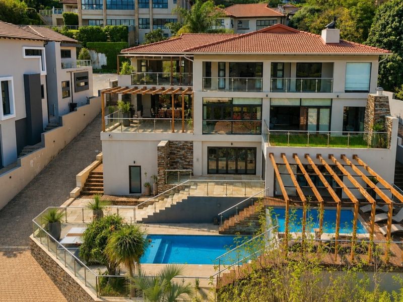 Aerial view of a multi-level luxury residence featuring a swimming pool, timber pergolas, expansive terraces, and modern glass balustrades.