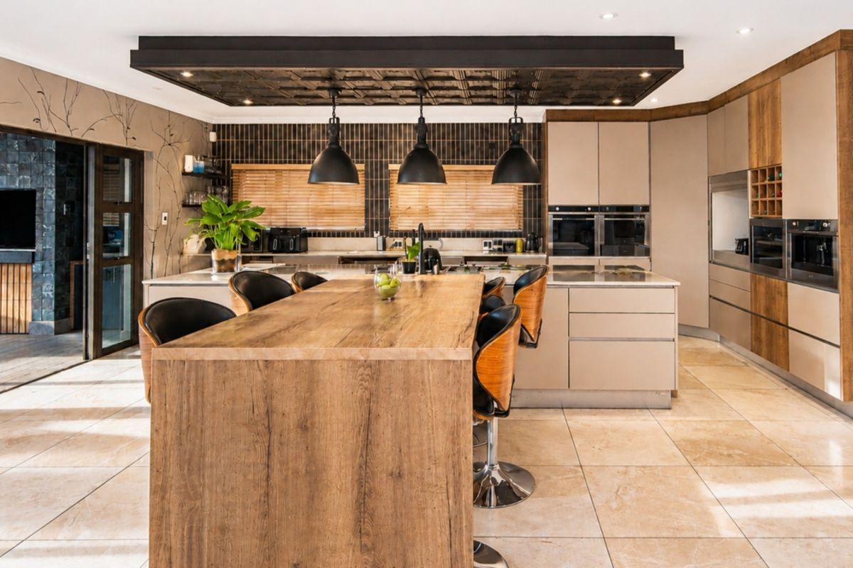 Modern kitchen featuring a large timber island, integrated appliances, stone countertops, and a distinctive drop ceiling with pendant lighting.