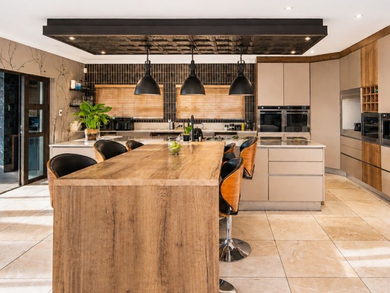 Modern kitchen featuring a large timber island, integrated appliances, stone countertops, and a distinctive drop ceiling with pendant lighting.