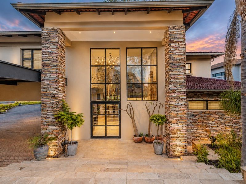 Impressive front entrance featuring stone-clad pillars, large steel-framed glass doors, and high-quality travertine tiling under a covered porch area.