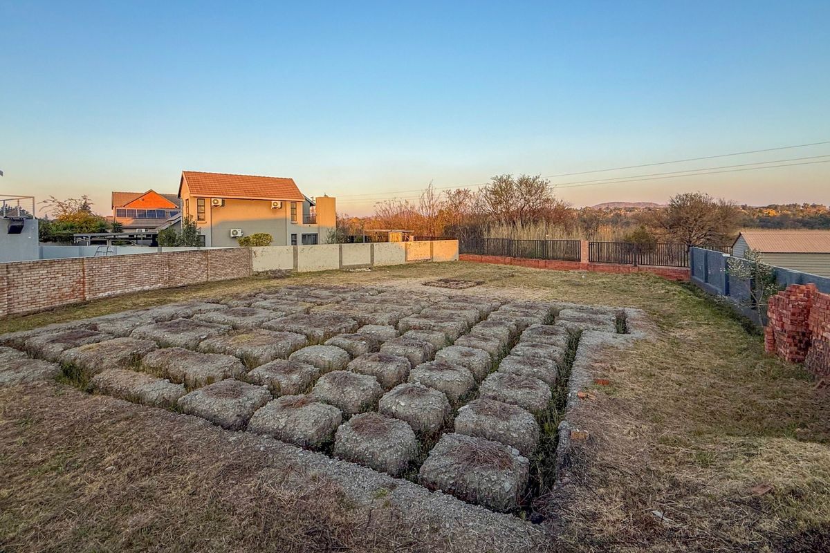 Vacant residential land featuring an exposed concrete foundation grid, enclosed by brick and metal boundary walls in a suburban setting.