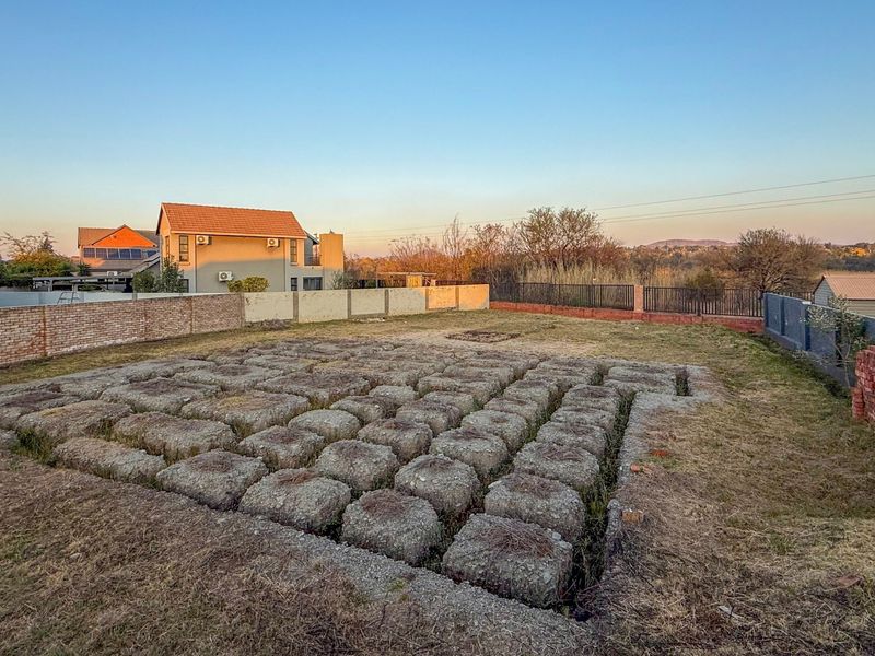 Vacant residential land featuring an exposed concrete foundation grid, enclosed by brick and metal boundary walls in a suburban setting.