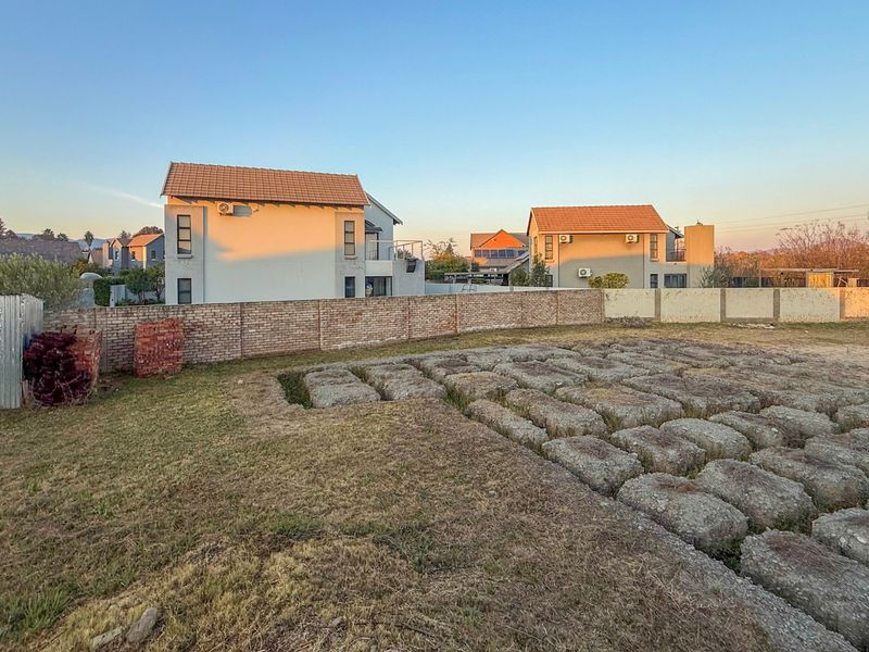 A vacant residential plot featuring a brick boundary wall, a small corrugated metal shed, and a series of concrete foundation blocks on the ground.