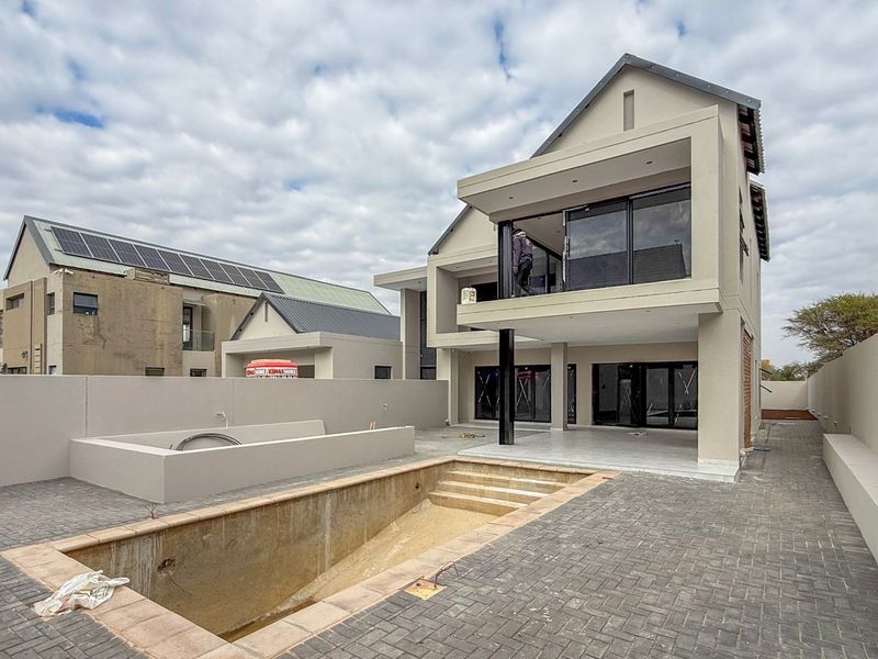 Rear view of a modern double-story house featuring a paved patio, balcony, and an unfinished swimming pool area.
