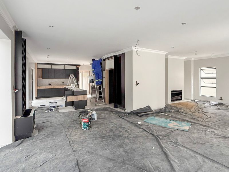 Spacious open-plan living and kitchen area currently undergoing final finishing touches, featuring modern cabinetry, a central island, and a built-in fireplace.