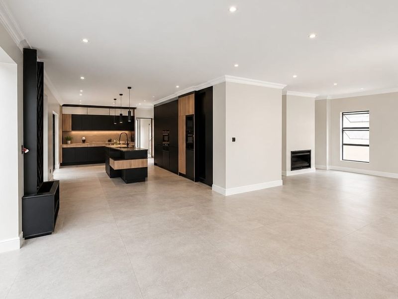 Spacious open-plan living area featuring a modern kitchen with a central island, sleek cabinetry, and a built-in fireplace, finished with neutral floor tiles.