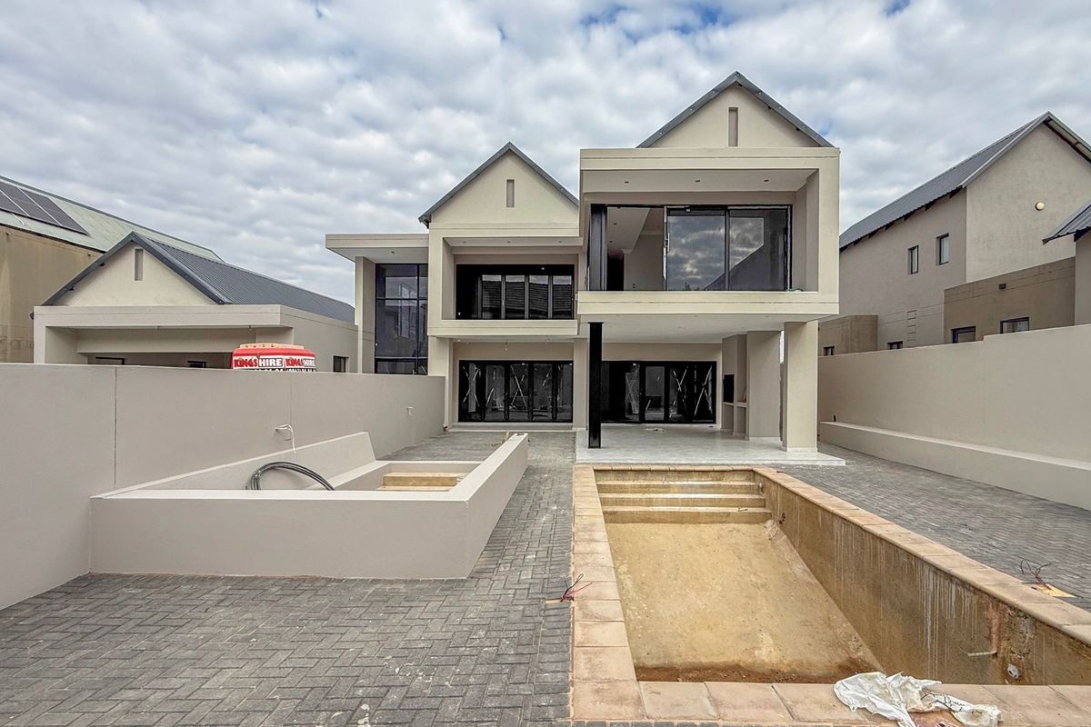 Rear view of a modern double-story house featuring a paved patio, balcony, and an unfinished swimming pool area.